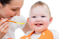 young mother spoon-feeding happy daughter